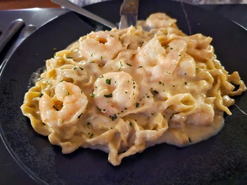 A blue plate with pasta in a white cream sauce, topped with shrimp.